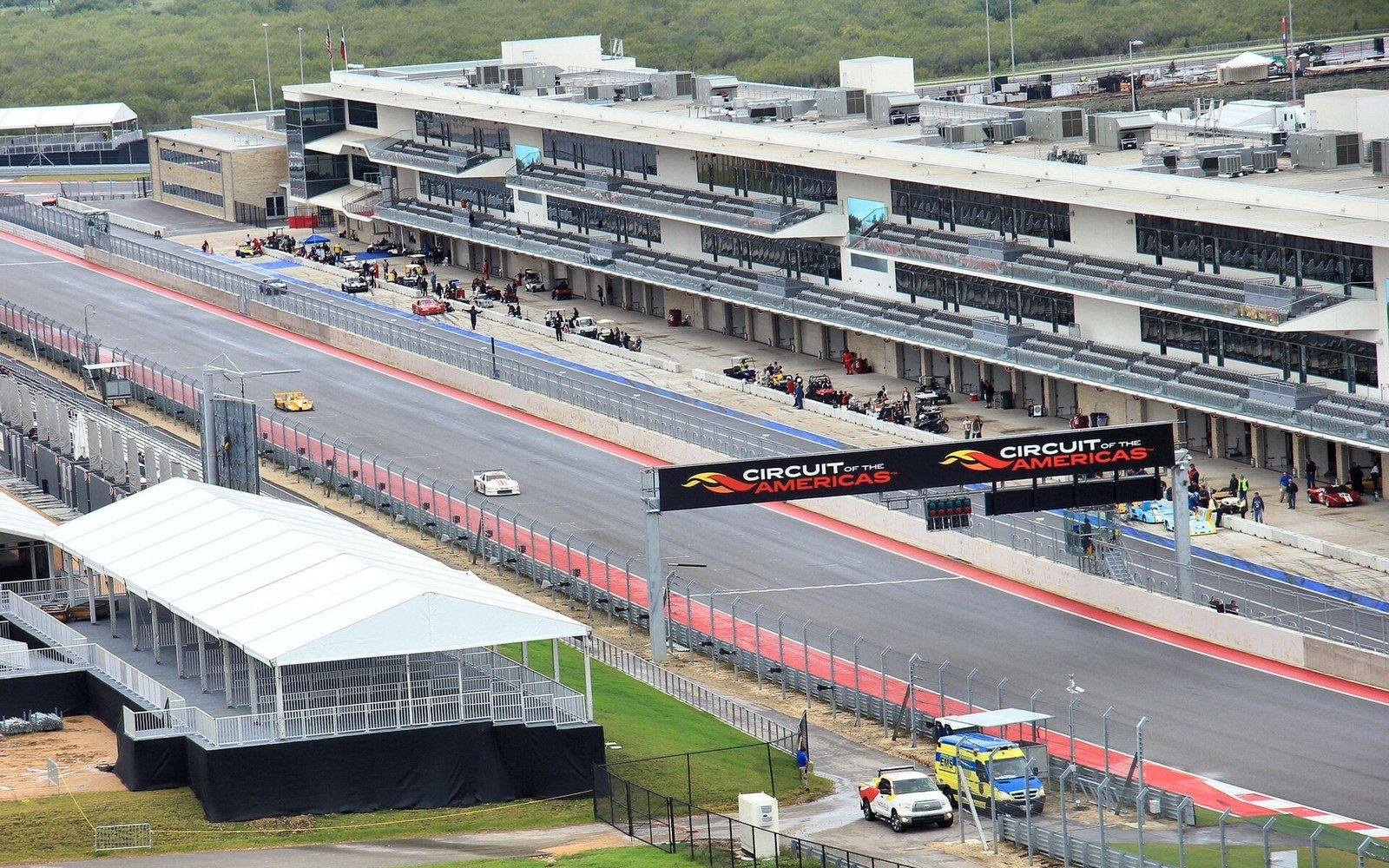 Circuit of the Americas paddock under race-day sun, tyre warmers on a row of superbike rear wheels, adult crew members in branded kit working in the background