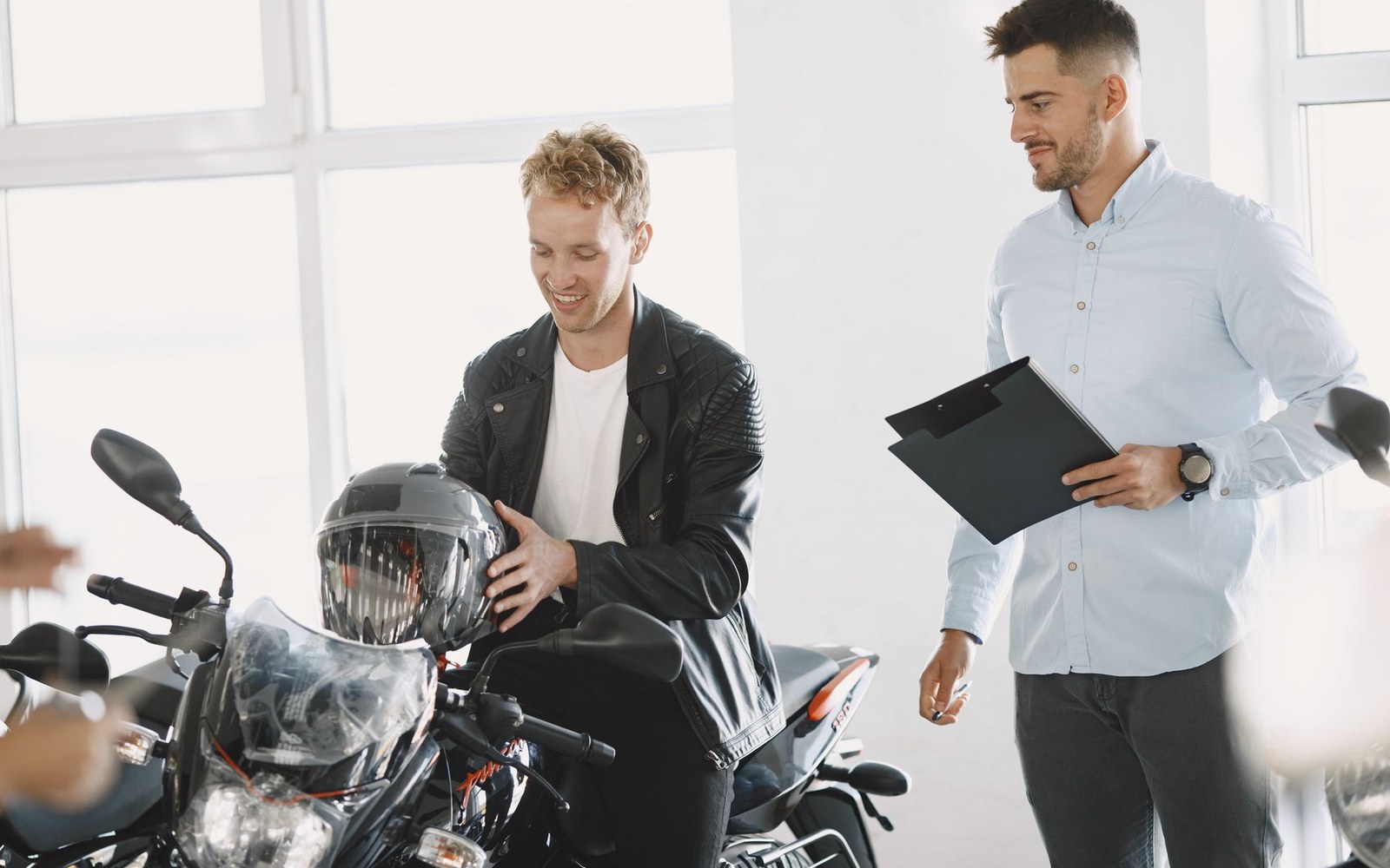Dealership showroom floor shot straight on, a row of five motorcycles of mixed displacement parked at an angle, a single adult salesperson standing at the far end