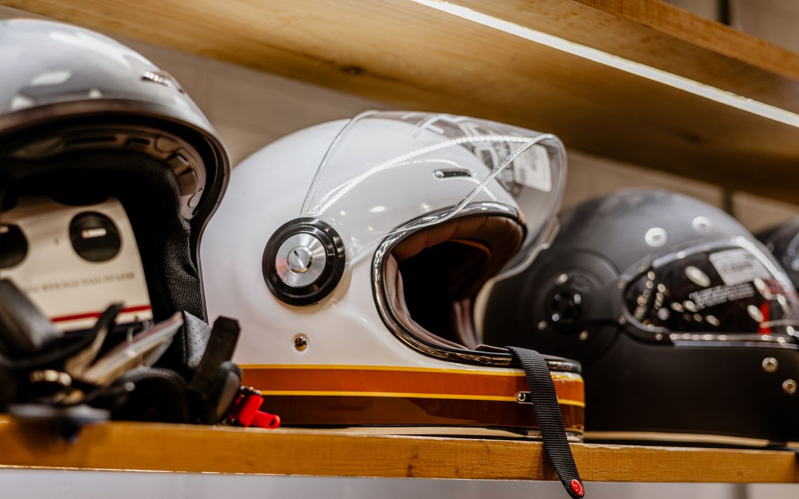 Full-face helmet resting on a motorcycle fuel tank, ECE 22.06 certification label visible on the rear, workshop wall out of focus behind