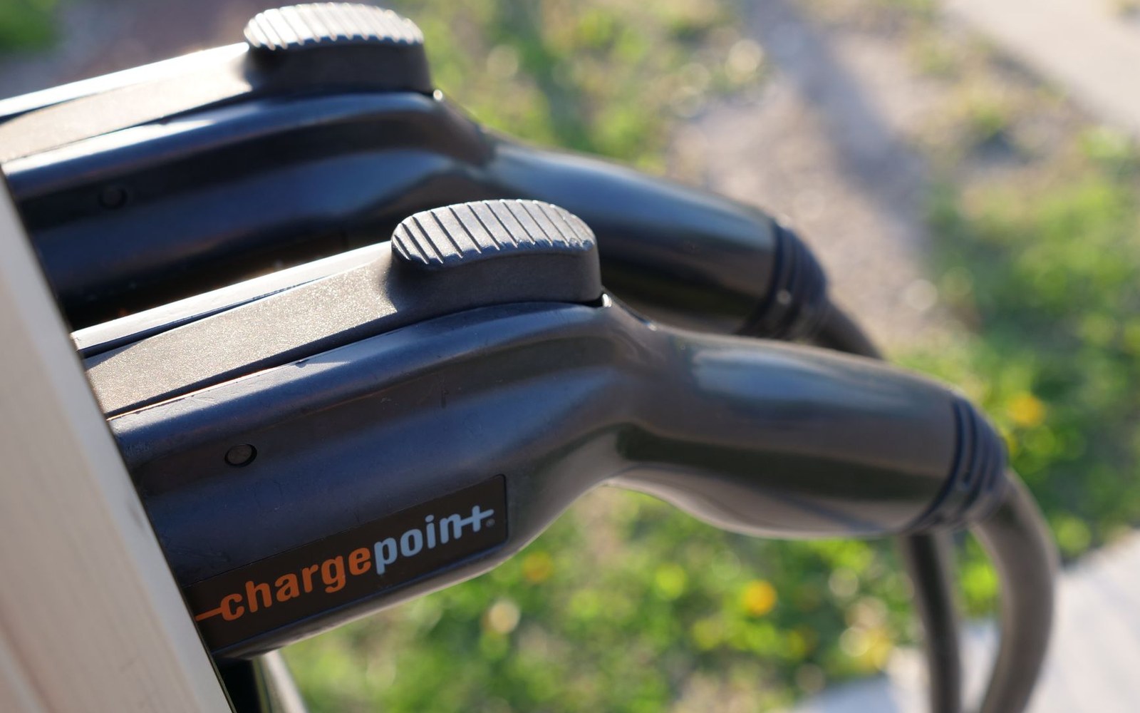 Electric motorcycle plugged into a DC fast-charger, charging indicator illuminated, industrial exterior setting, no rider present