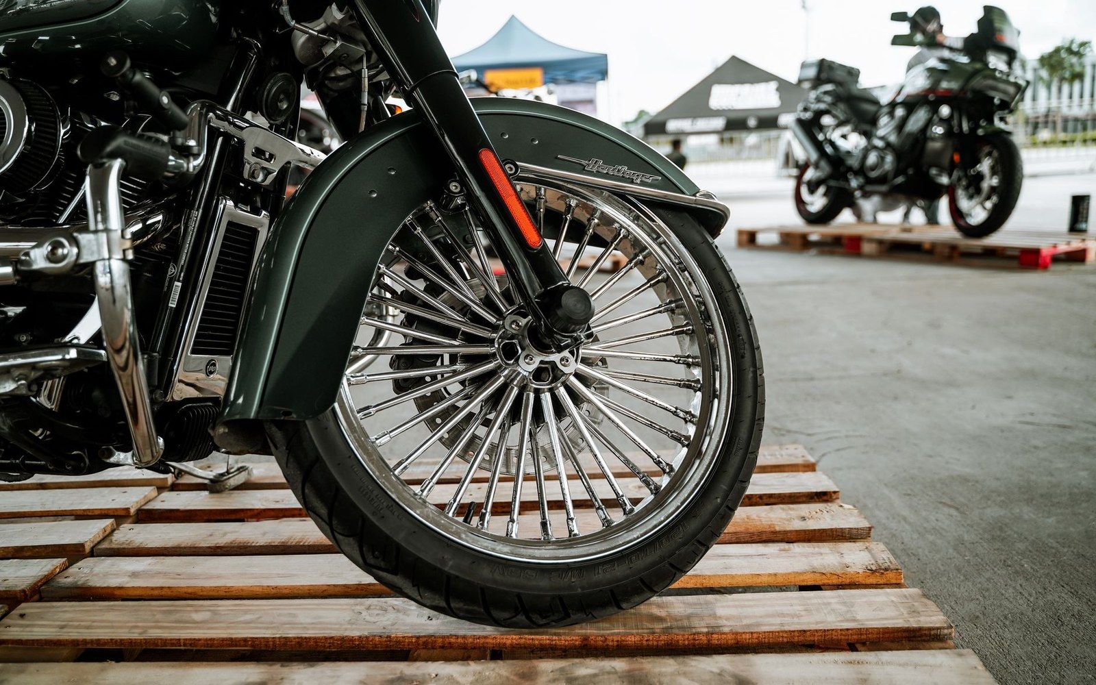 Close-up of a Harley-Davidson's chrome spoked front wheel and fork on wooden pallets