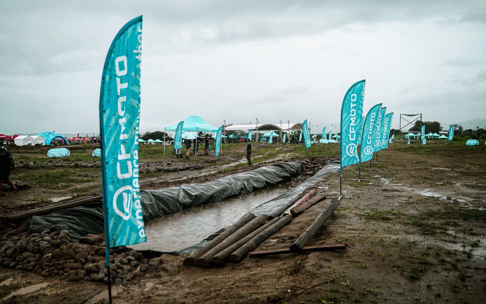 CFMoto branded flags line a muddy outdoor event site under overcast skies