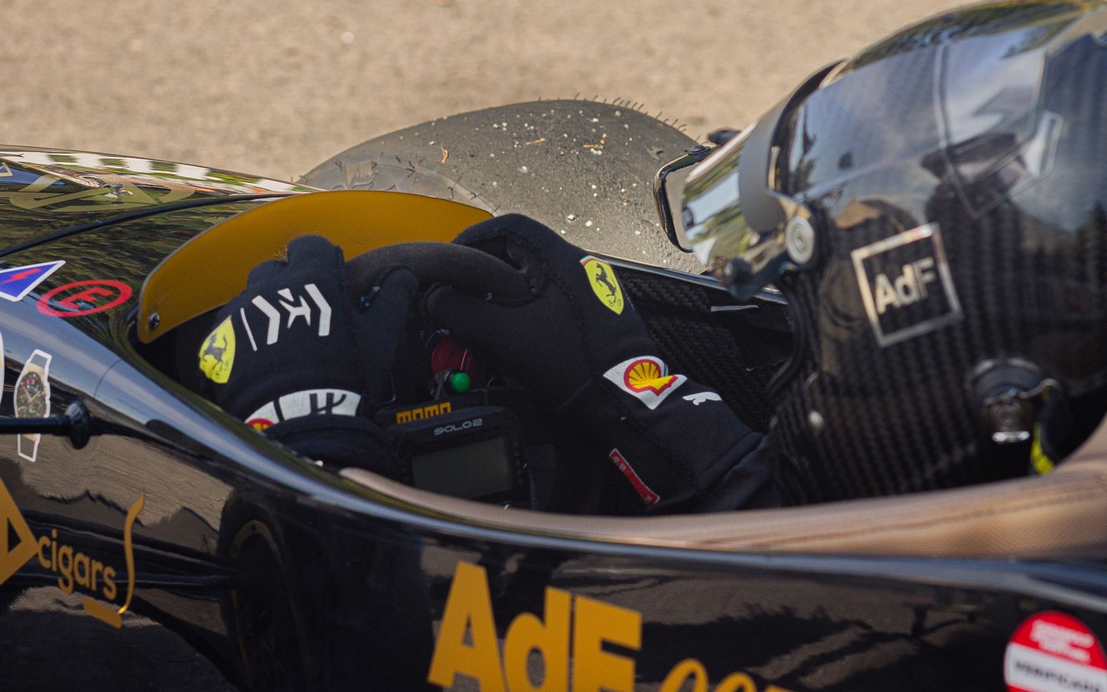 Gloved hand rests on a race car's steering wheel beside a helmeted driver's head