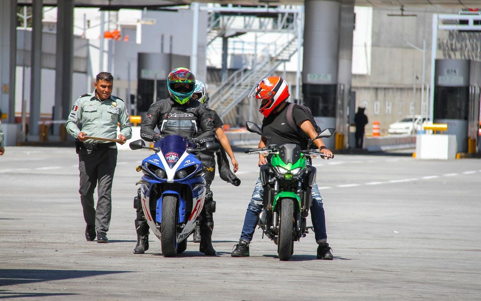 Two helmeted riders on sport motorcycles stop as an officer checks documents at a toll booth