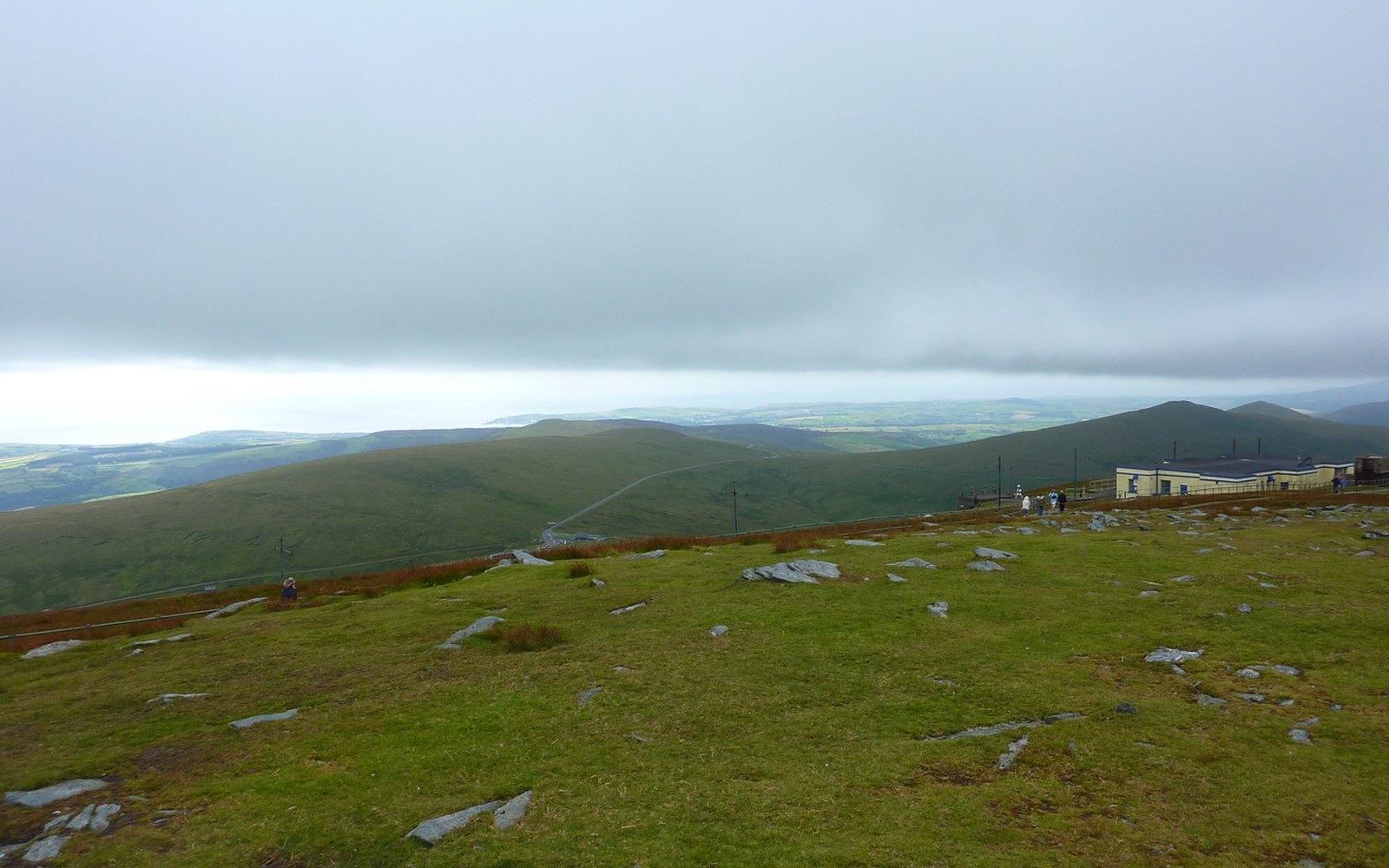 Rocky grassy hilltop overlooking rolling hills and a distant coastline under heavy cloud
