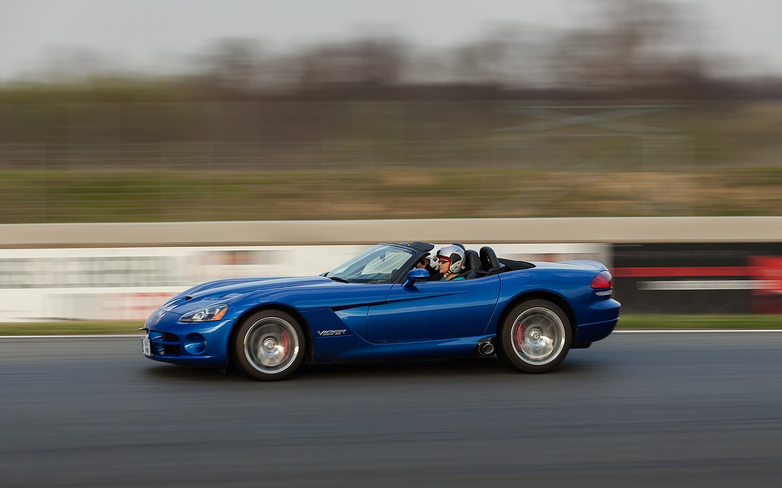 A blue Dodge Viper convertible speeds down a racetrack with a helmeted driver