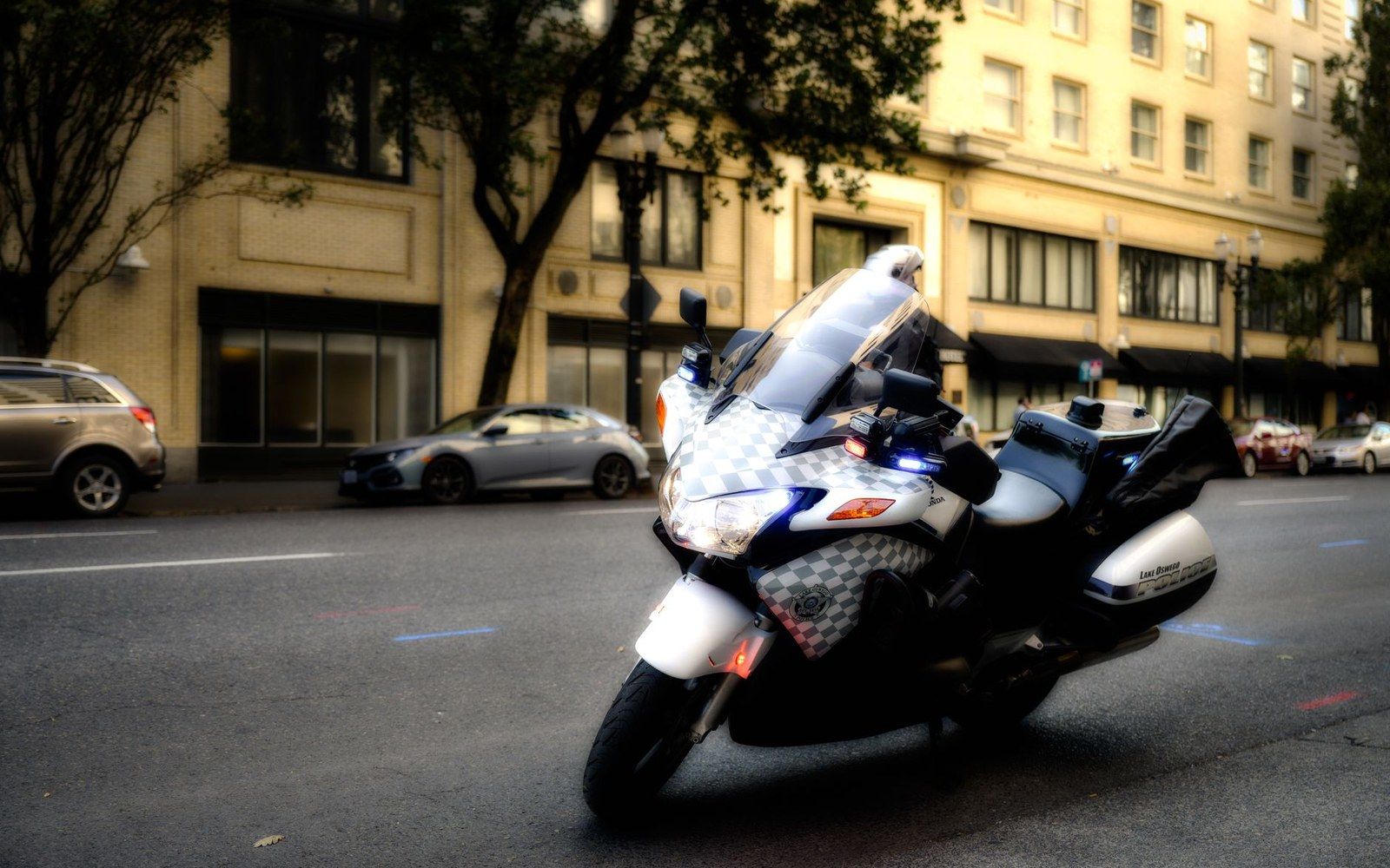 A police motorcycle with flashing lights parked on a city street lined with buildings