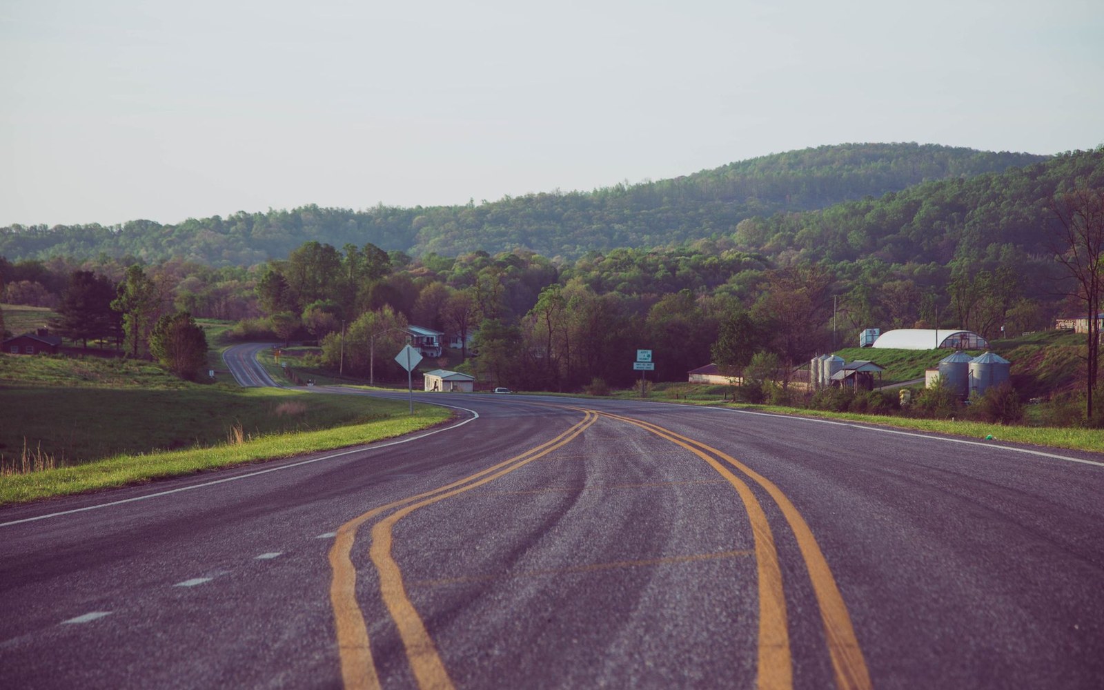 Ranch Road 337 running straight to a Hill Country horizon under hard midday Texas light, asphalt heat shimmer, cedar and live oak on both sides